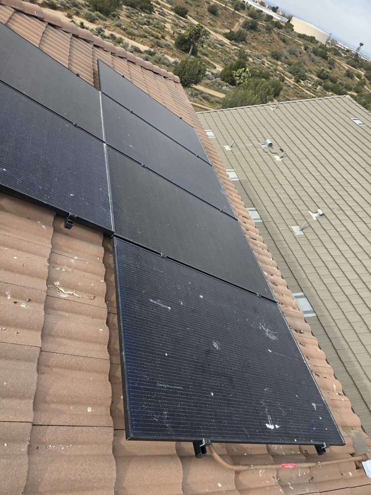 Dusty solar panels on a roof with desert and Joshua trees behind before cleaning